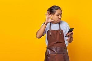 Retrato de hombre asiático de aspecto serio tratando de escuchar una conversación secreta y sosteniendo el teléfono inteligente foto