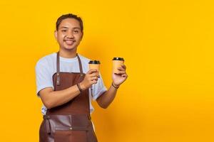 Portrait of cheerful barista man holding two paper coffee cups for you to choose isolated on yellow background photo