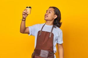 Retrato de hombre guapo vestido con delantal mirando una taza de café que se celebra aislado sobre fondo amarillo foto