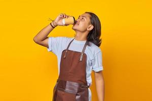 Portrait of handsome man wearing apron enjoying a cup of coffee on yellow background