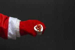 Close-up of Santa Claus in red mittens holding a gift on a black background copy space photo