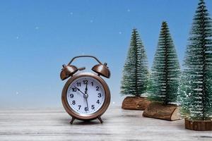Christmas background with small Christmas trees and vintage alarm clock on a wooden background with lights. Close