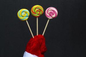 Merry Christmas and Happy New Year concept. Close up on black background santa claus hand holding candy on stick, copy space photo