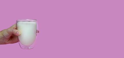 female hand holding a glass with fresh milk, on a pink background,fortified drink, calcium,banner photo