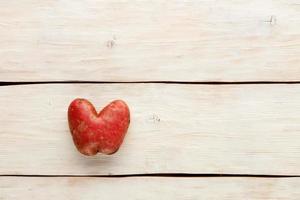 patata fea en forma de corazón sobre un fondo de madera blanca. concepto de desperdicio de vegetales o alimentos. vista superior, primer plano. foto