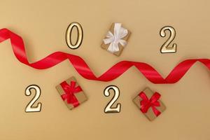 New Year 2022. Top view New Year mockup on beige background red ribbon, gift box, gold numbers and multicolored sparkles. Layout of postcards, invitations. photo