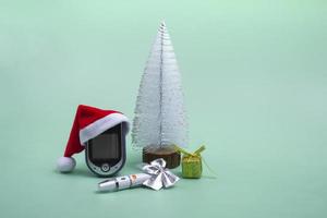 A glucometer in a New Year's hat, a lancet, a gift and a white spruce on a blue background. Medical concept. Postcard, card. New Year's and Christmas. photo