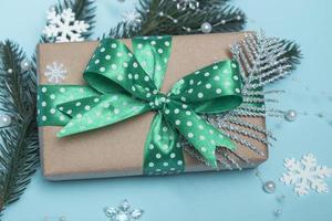 Merry Christmas and Happy New Year. Gift with a green ribbon with polka dots and ornaments on a blue background. Holiday card close up photo