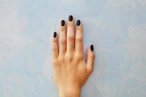 Nails with a beautiful black manicure with glitter on a female hand on a marble background of a blue wall in blur. photo