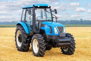 Tractor agrícola de ruedas con campo de trigo amarillo cosechado y cielo nublado en el fondo.28, 07, 21 en Kiev, Ucrania foto