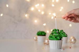 Cupcakes con forma de árbol de Navidad, rodeados de adornos festivos y luces de fondo foto
