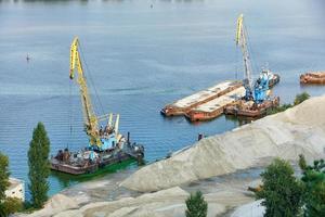 transporte y equipo industrial fluvial. Grúas industriales flotantes cargan arena de río en barcazas metálicas para su posterior transporte. foto