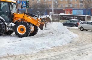 A large ladle of a yellow bulldozer shovels snow from a city road during a snowfall. photo