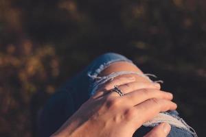 Beautiful twisted silver wedding ring set on young adult female. Sun shining and hand and jeans. photo