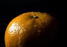 Gota de agua sobre la superficie brillante de frescura naranja sobre fondo negro foto