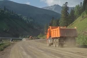 camión volquete cargado conduciendo por un camino de tierra en las montañas. foto