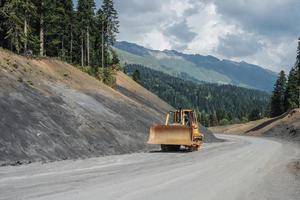 Excavadora sobre orugas conduciendo por un camino de tierra en las montañas. foto