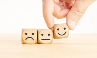 Customer service evaluation concept. Hand picking the happy face emoticon on wooden block photo
