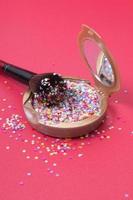 Makeup powder and cosmetic brush with glitter stars on red background photo