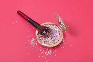 Makeup powder and cosmetic brush with glitter stars on red background photo