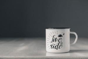 Enamel white metal mug with black line on edge with inscription on white wooden table photo