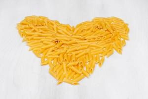 Pasta penne rigate in the shape of a heart on a white background wooden table photo