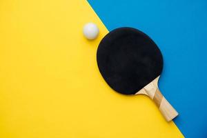 Tenis de mesa o raqueta de ping pong y pelota sobre fondo azul y amarillo foto