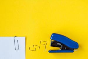 Blue stapler with metal staples and paper clip on yellow background photo