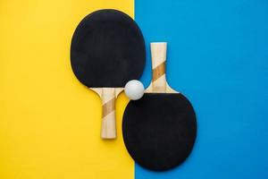 Dos raquetas de tenis de mesa o ping pong y pelota sobre fondo azul y amarillo foto