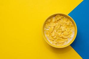 Copos de maíz con leche en el recipiente amarillo sobre fondo azul y amarillo foto