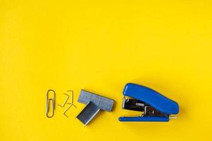 Grapadora azul con grapas de metal y clip de papel sobre fondo amarillo foto