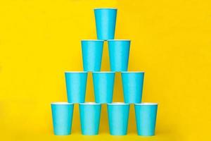 Pyramid of blue paper disposable cups on yellow background photo