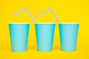 Colocación de vasos de papel azul en una línea con pajitas de plástico de colores para beber sobre fondo amarillo