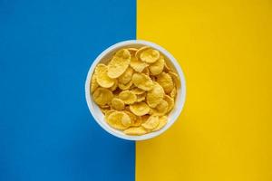 Cornflakes in white bowl on blue and yellow background photo