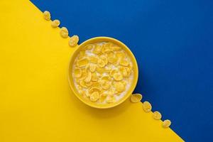 Copos de maíz con leche en el recipiente amarillo sobre fondo azul y amarillo