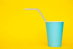 Blue paper cup with drinking colored plastic straw on yellow background photo