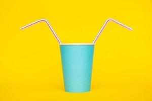 Vaso de papel azul con pajitas de plástico de colores para beber sobre fondo amarillo
