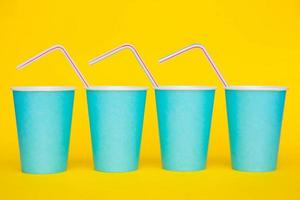Colocación de vasos de papel azul en una línea con pajitas de plástico de colores para beber sobre fondo amarillo
