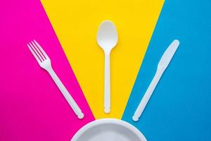 tenedor, cuchillo, cuchara y plato de plástico blanco sobre fondo multicolor foto