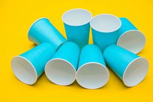 Muchos vasos desechables de papel azul sobre fondo amarillo