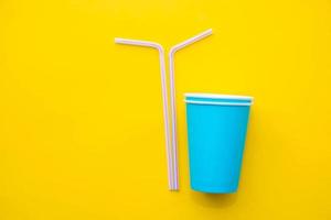 Blue paper cups with drinking colored plastic straws on yellow background photo