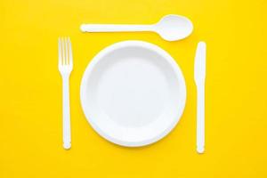 tenedor, cuchillo, cuchara y plato de plástico blanco sobre fondo amarillo