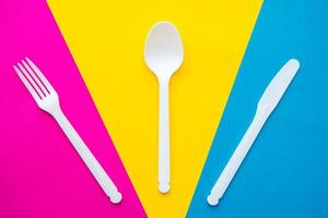 Plastic white fork, spoon and knife on multicolored background photo