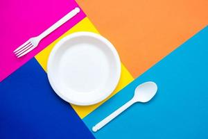 Tenedor, cuchara y plato de plástico blanco sobre fondo multicolor foto