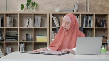 bella donna d'affari di etnia asiatica lavora su e-commerce utilizzando laptop, comunicazione internet in ufficio di piccole imprese. persona attraente, tradizionalmente abiti islamici indossando l'hijab. video