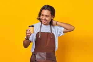 Retrato de hombre guapo vestido con delantal mirando una taza de café que se celebra aislado sobre fondo amarillo foto