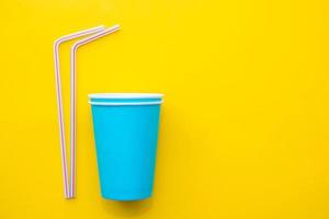 Blue paper cups with drinking colored plastic straws on yellow background