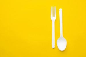 Plastic white spoon and fork on yellow background photo