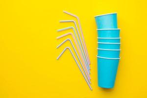Blue paper cups with drinking colored plastic straws on yellow background