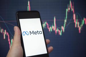 META logo on smartphone screen with hand hold and crypto currency or stocks graph charge trading screen on background. New facebook company logo meta metaverse. Bangkok Thailand, December 2, 2021 photo